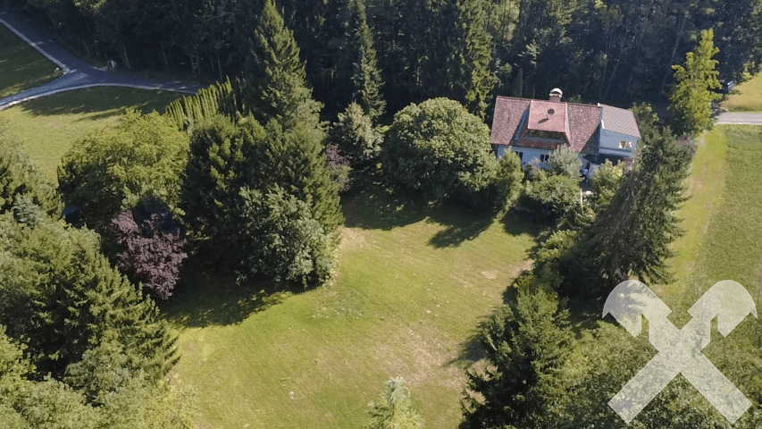 Weitläufige Luftaufnahme des Hauses mit großem Garten und umliegenden Wäldern unter blauem Himmel.