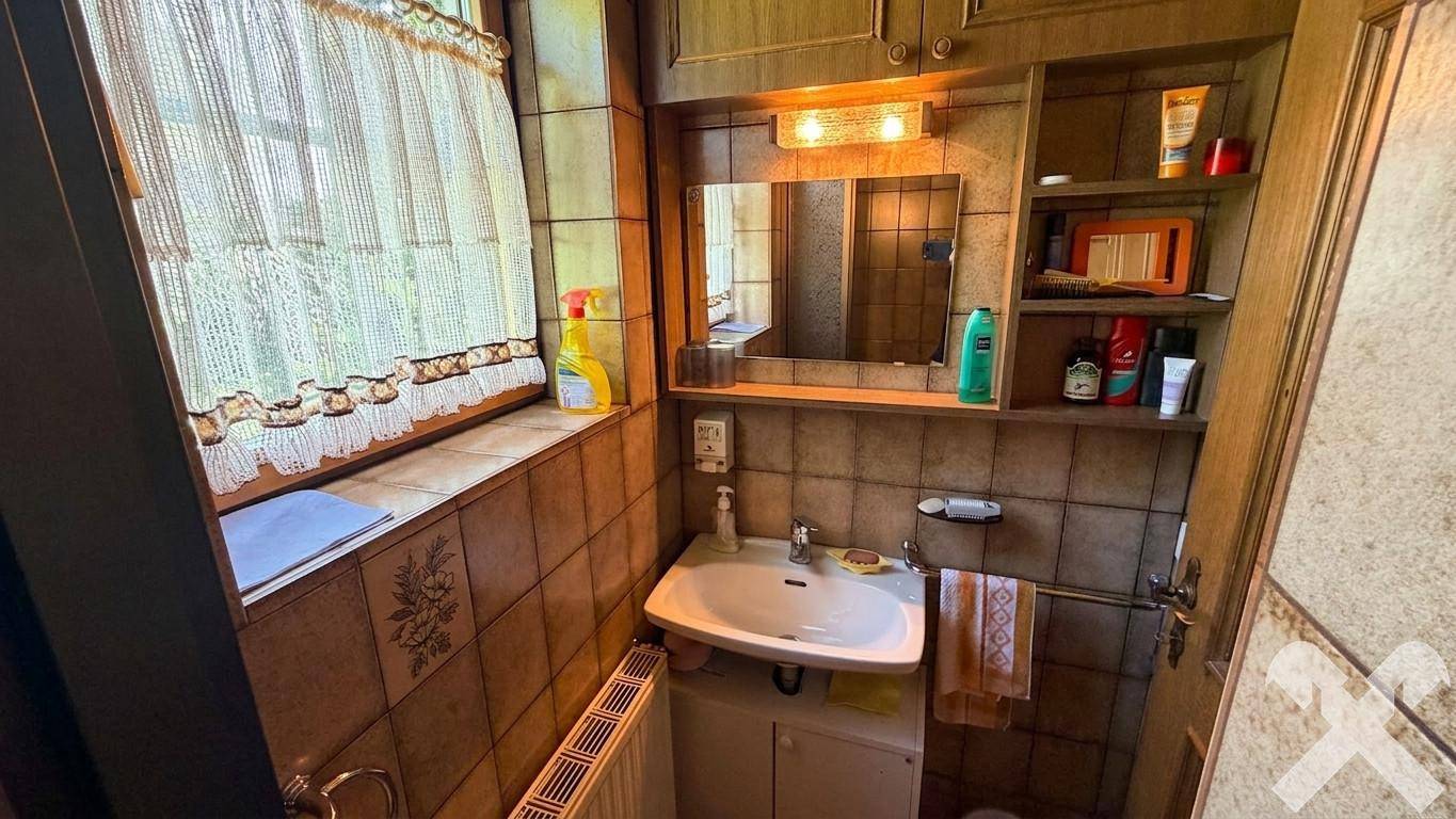 Kleines Badezimmer mit braunen Fliesen, Einzelwaschbecken und Fenster für Tageslicht.