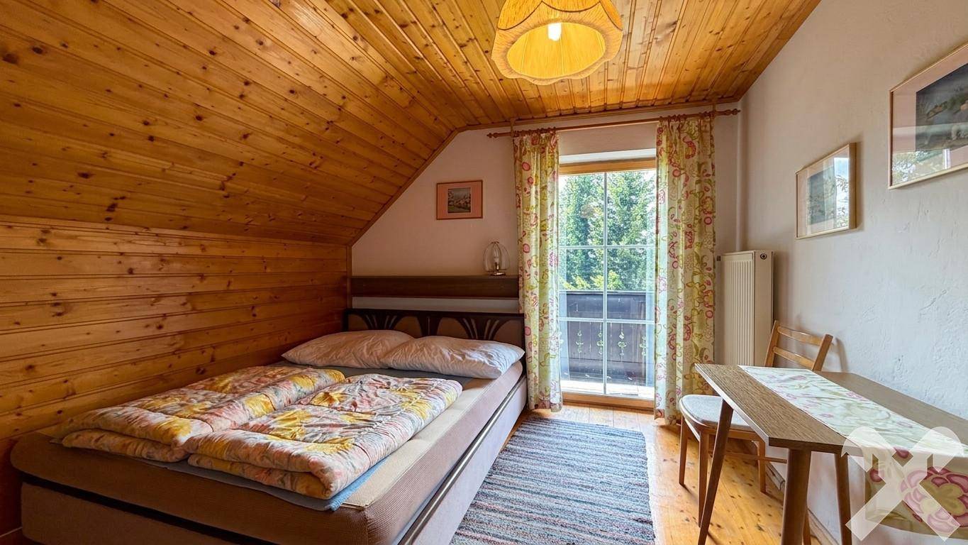 Gemütliches Schlafzimmer mit Dachschräge, Holzwänden und Zugang zu einem kleinen Balkon.