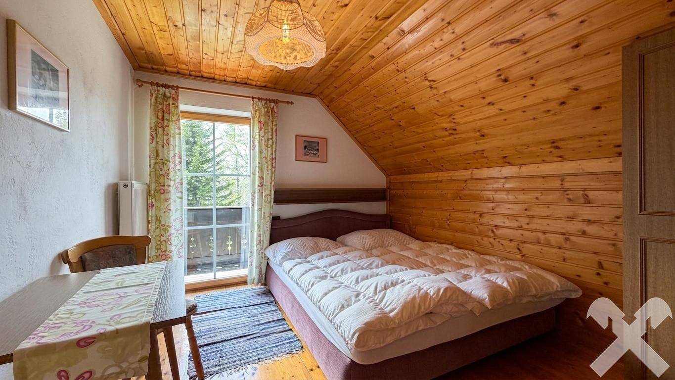 Helles Schlafzimmer mit Holzverkleidung, Dachschräge und direktem Balkonzugang.
