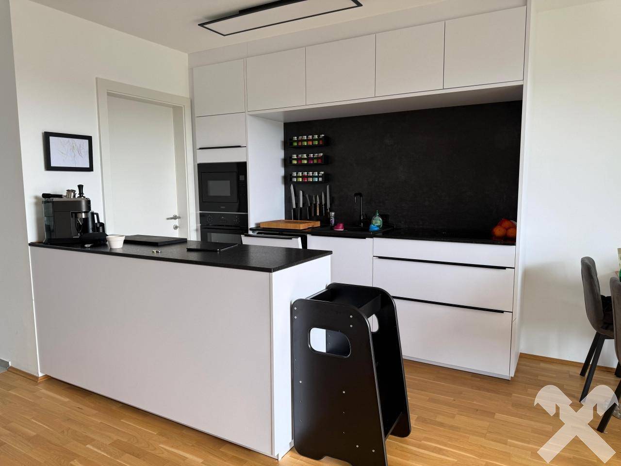 Moderne Einbauküche mit weißen Fronten, dunkler Arbeitsplatte und integrierten Geräten.