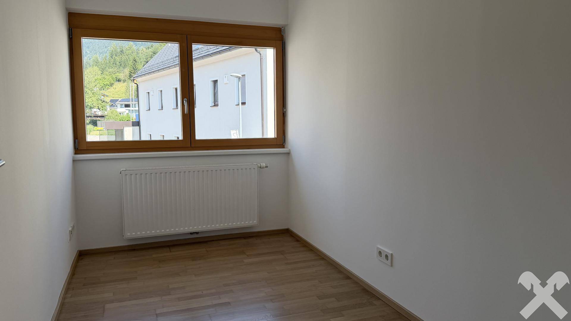 Kleineres, helles Schlafzimmer mit Holzparkettboden und einem Fenster mit Bergblick.