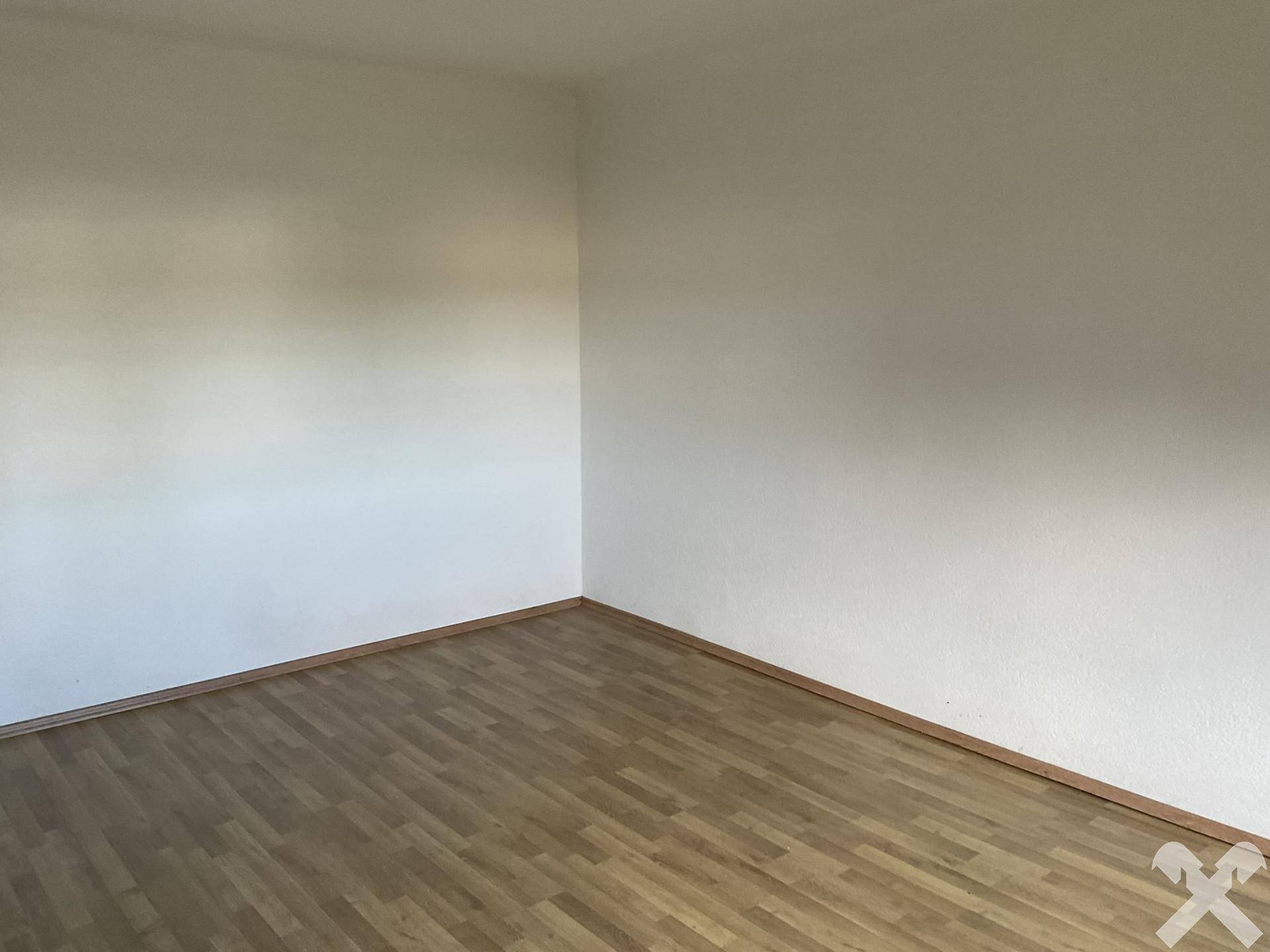 Ecke eines leeren Raumes mit hellen Wänden und Laminatboden, bietet eine neutrale Basis.
