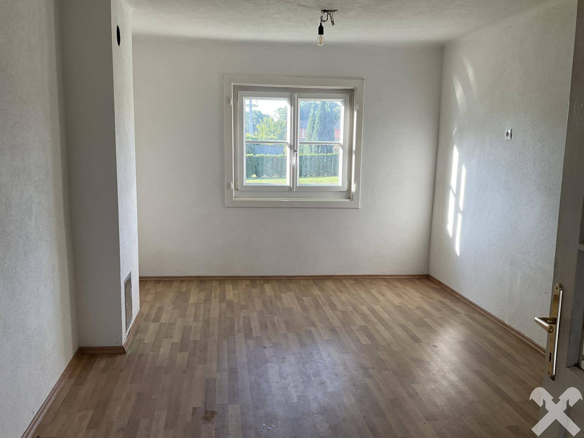 Heller Raum mit Laminatboden und Fensterblick ins Grüne, ideal als Wohn- oder Schlafzimmer.