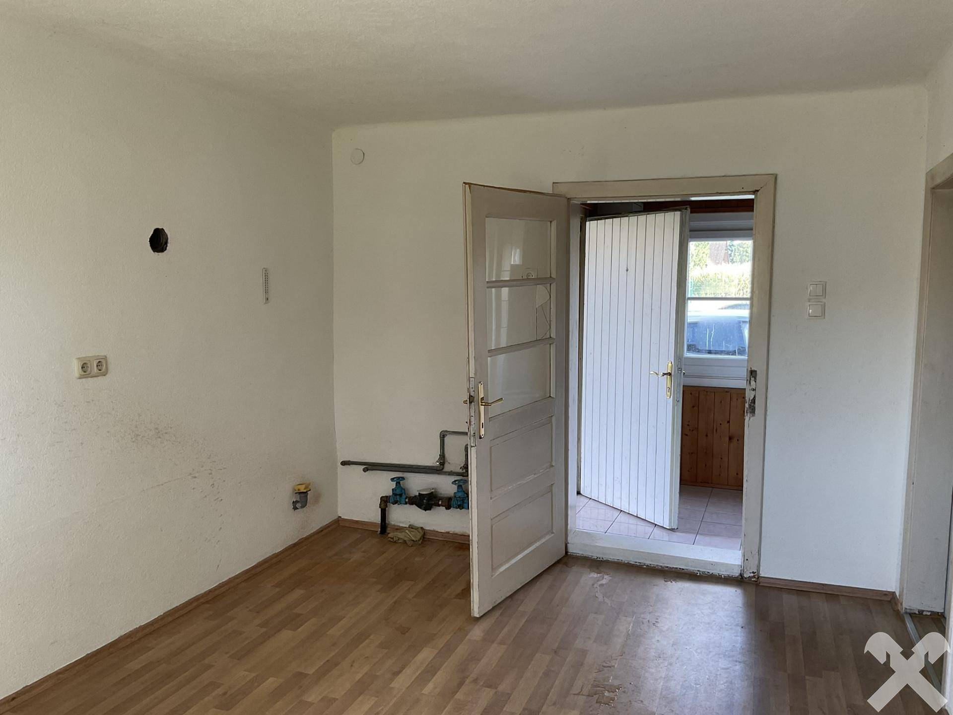 Leerer Raum mit sichtbaren Anschlüssen für eine Küche und Laminatboden, bereit zur Gestaltung.