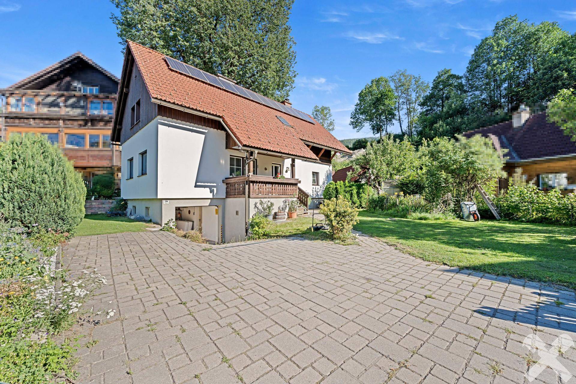 Ansicht des Einfamilienhauses von der Seite mit großzügiger gepflasterter Auffahrt und Gartenbereich.