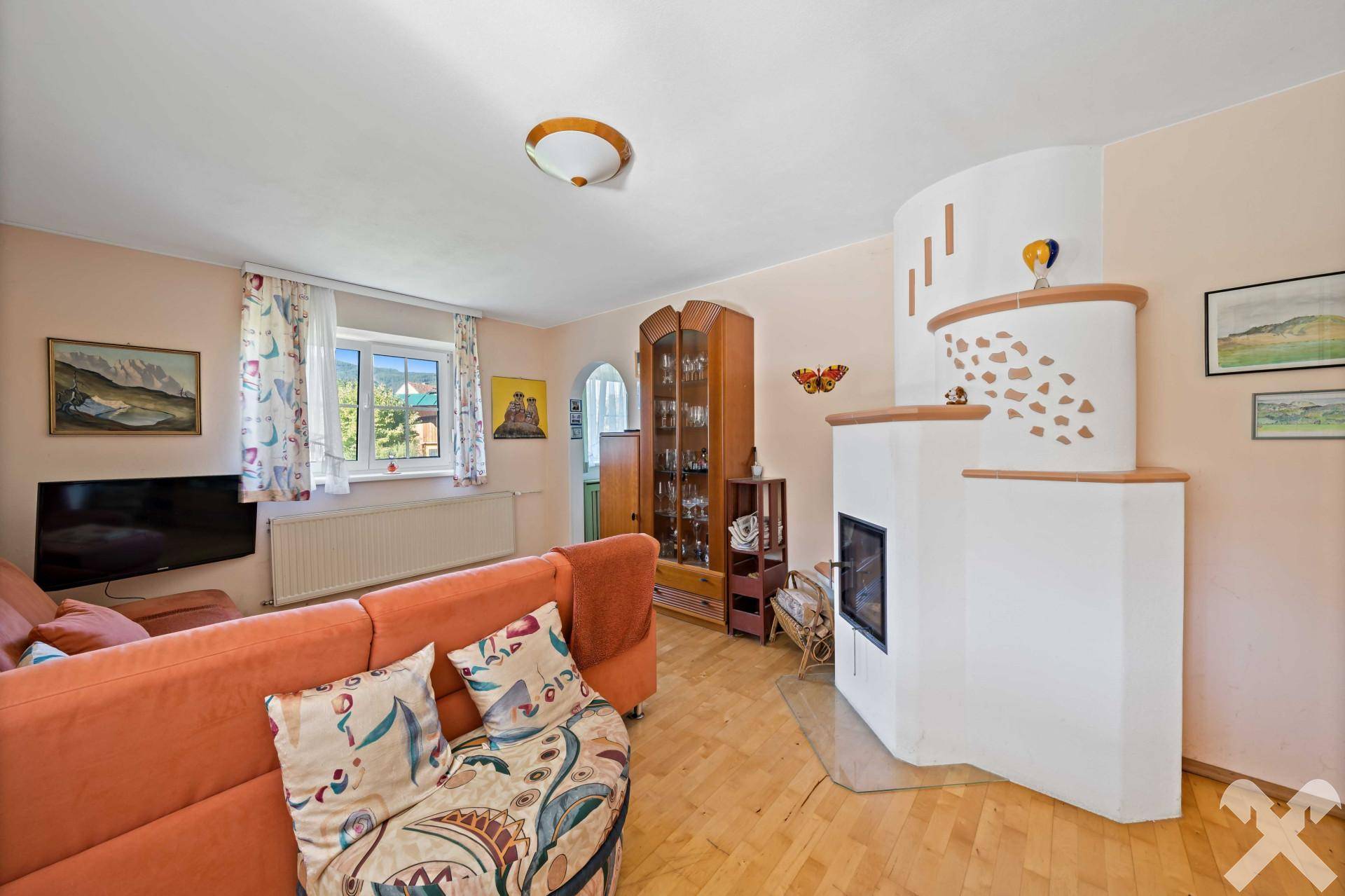 Helles Wohnzimmer mit traditionellem Kachelofen, bequemer Couch und Holzboden.