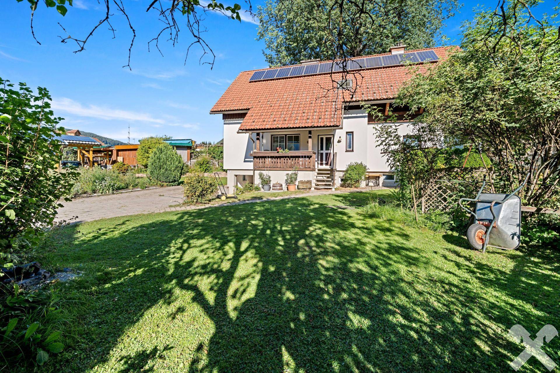 Vorderansicht des Hauses mit weitläufigem Rasen, Bäumen und einer sonnigen Gartenfläche.
