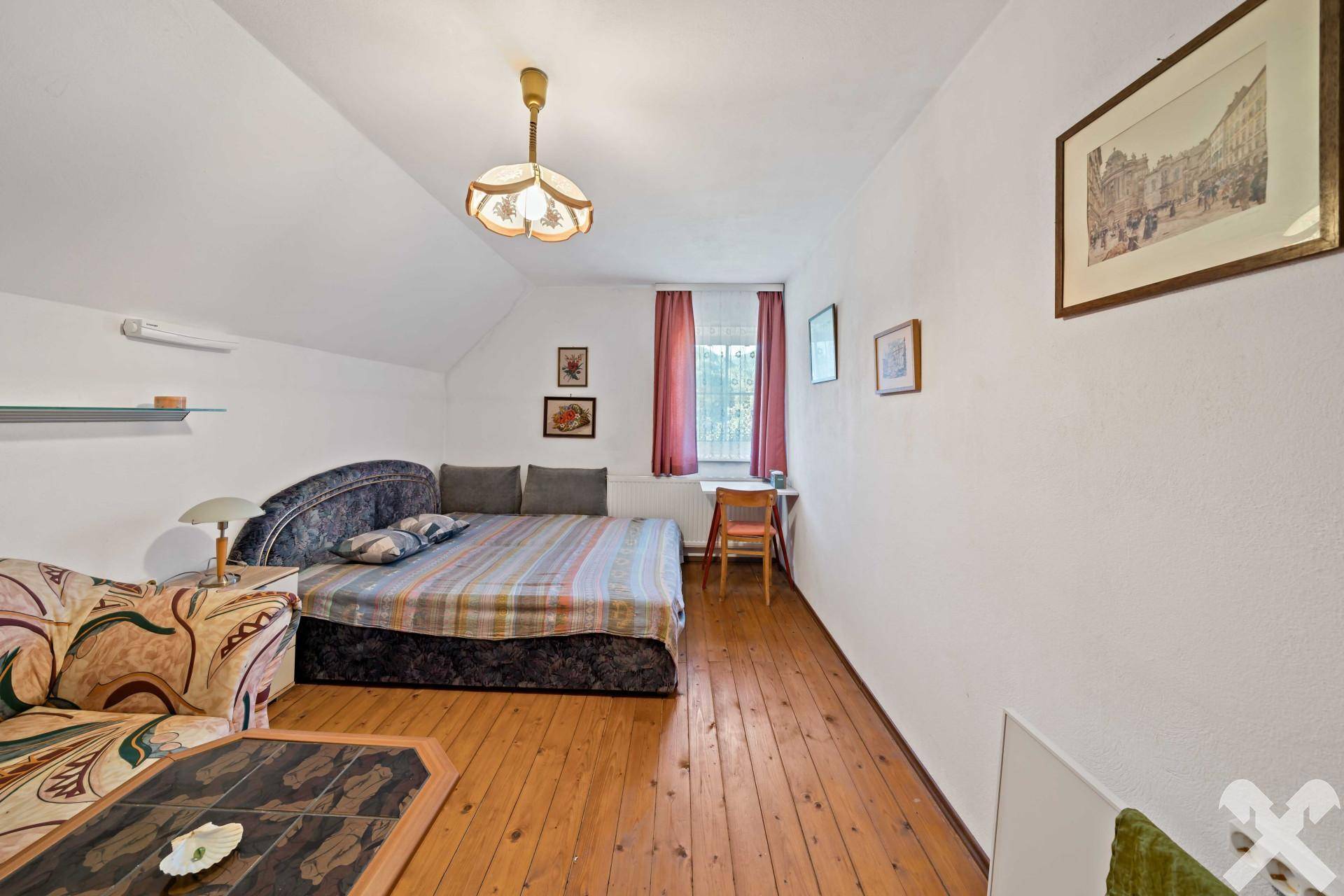 Helles Schlafzimmer mit Holzdielenboden, Bett und einem kleinen Schreibtisch am Fenster.