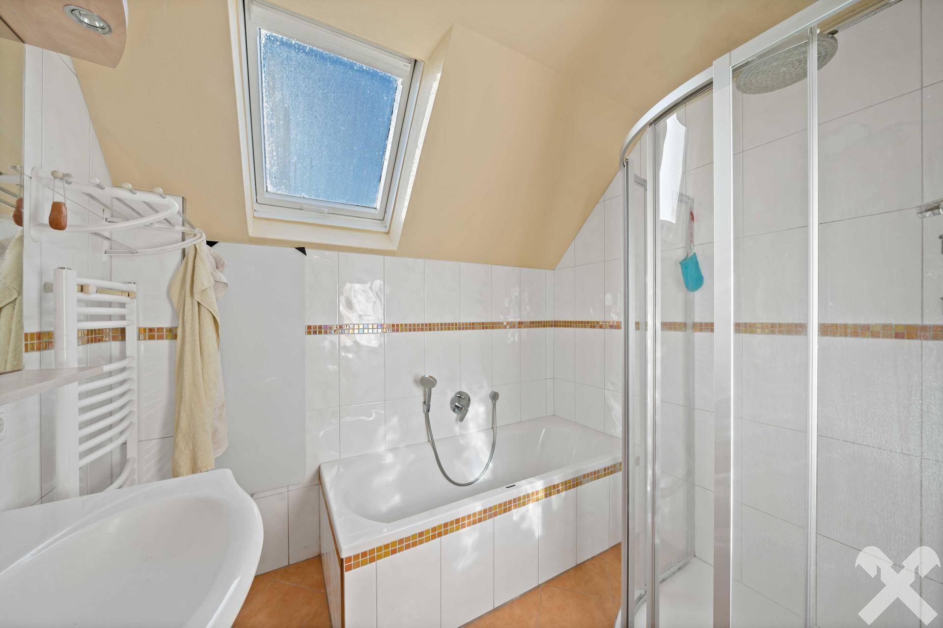 Badezimmer mit Badewanne, Duschkabine, Waschbecken und einem Dachfenster für Tageslicht.