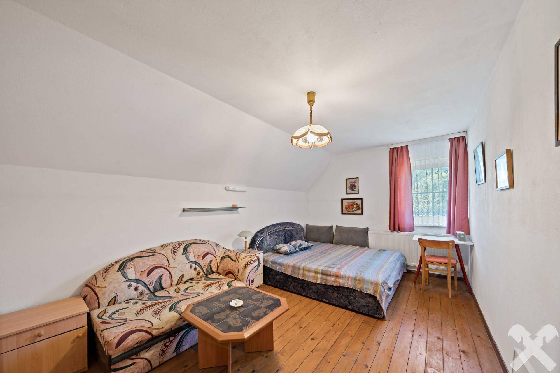 Gemütliches Schlafzimmer im Dachgeschoss mit Bett, Sofa und Holzdielenboden.