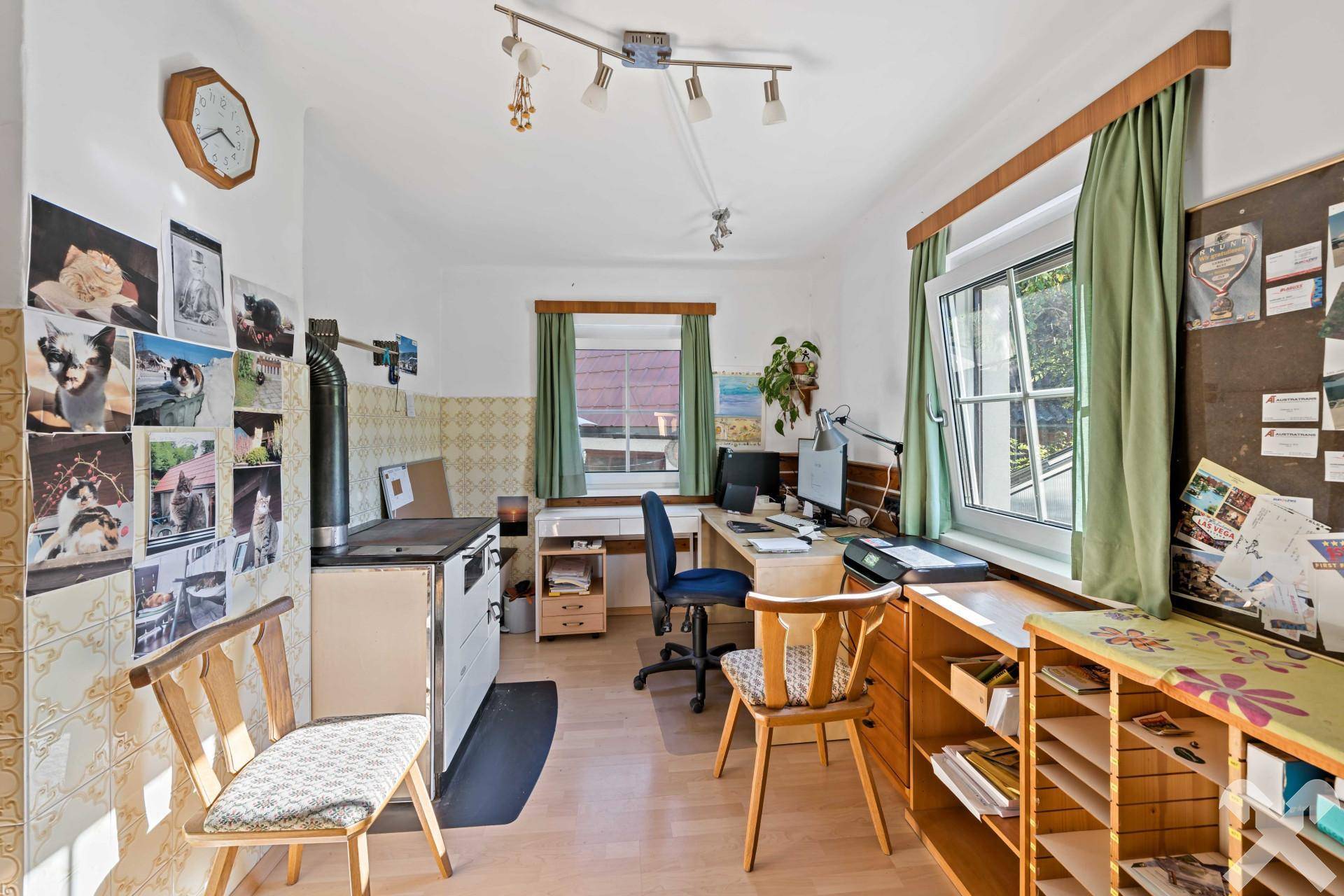 Arbeitszimmer mit Schreibtisch, Holzofen und Blick ins Grüne durch das Fenster.