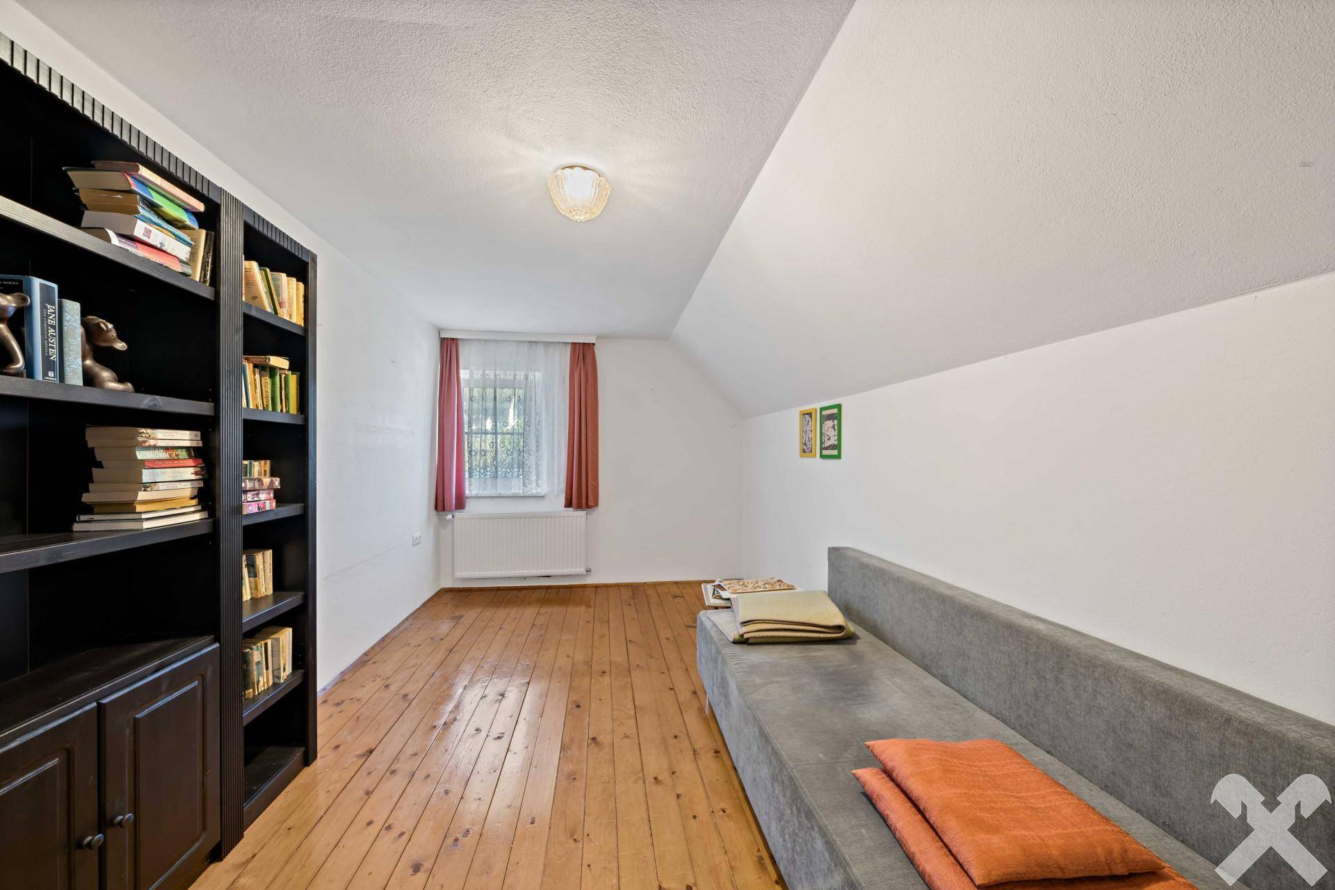 Geräumiger Raum mit langem Sofa, Bücherregal und Holzdielenboden im Dachgeschoss.