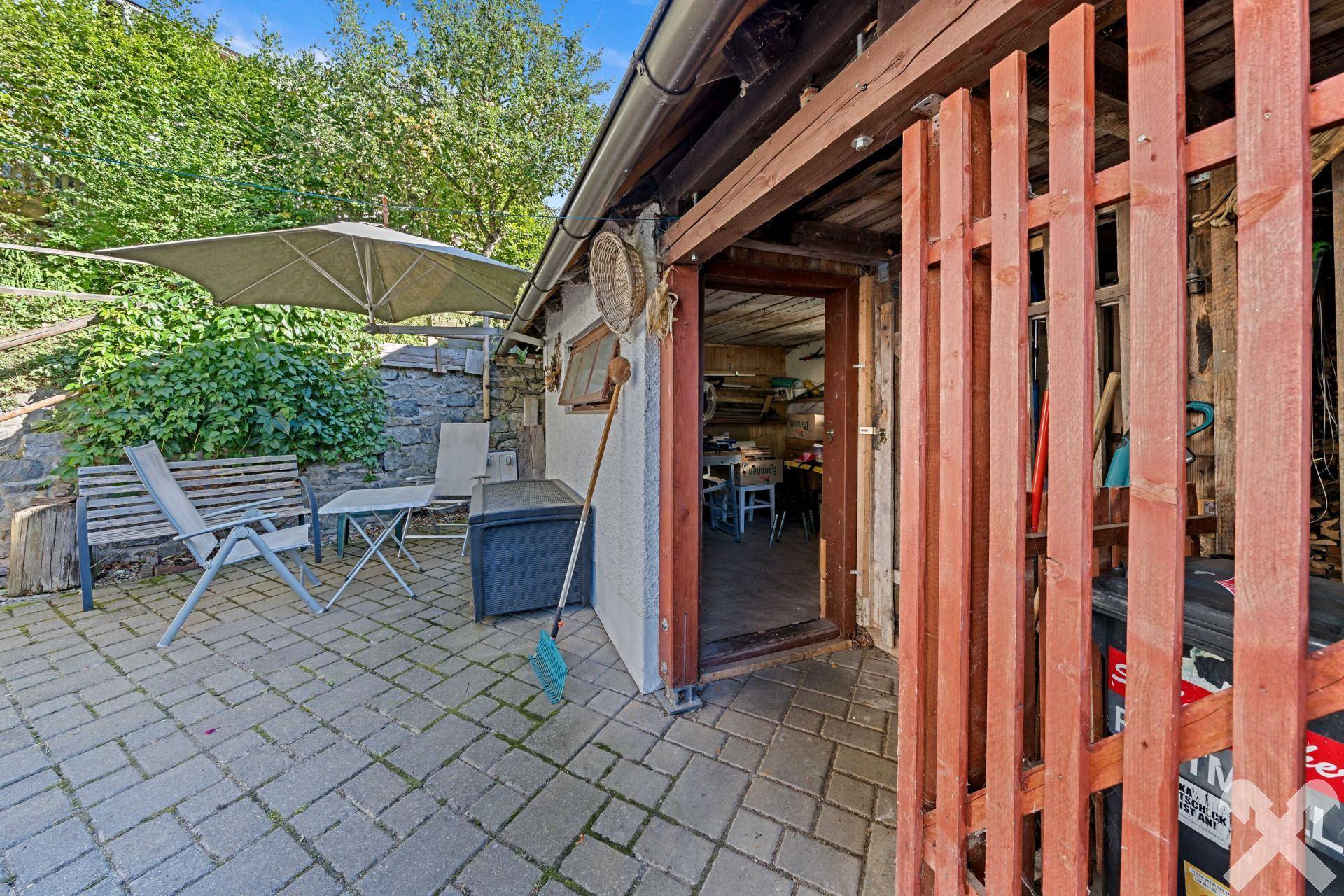 Gemütliche gepflasterte Terrasse mit Sitzgelegenheiten und Sonnenschirm im Außenbereich.