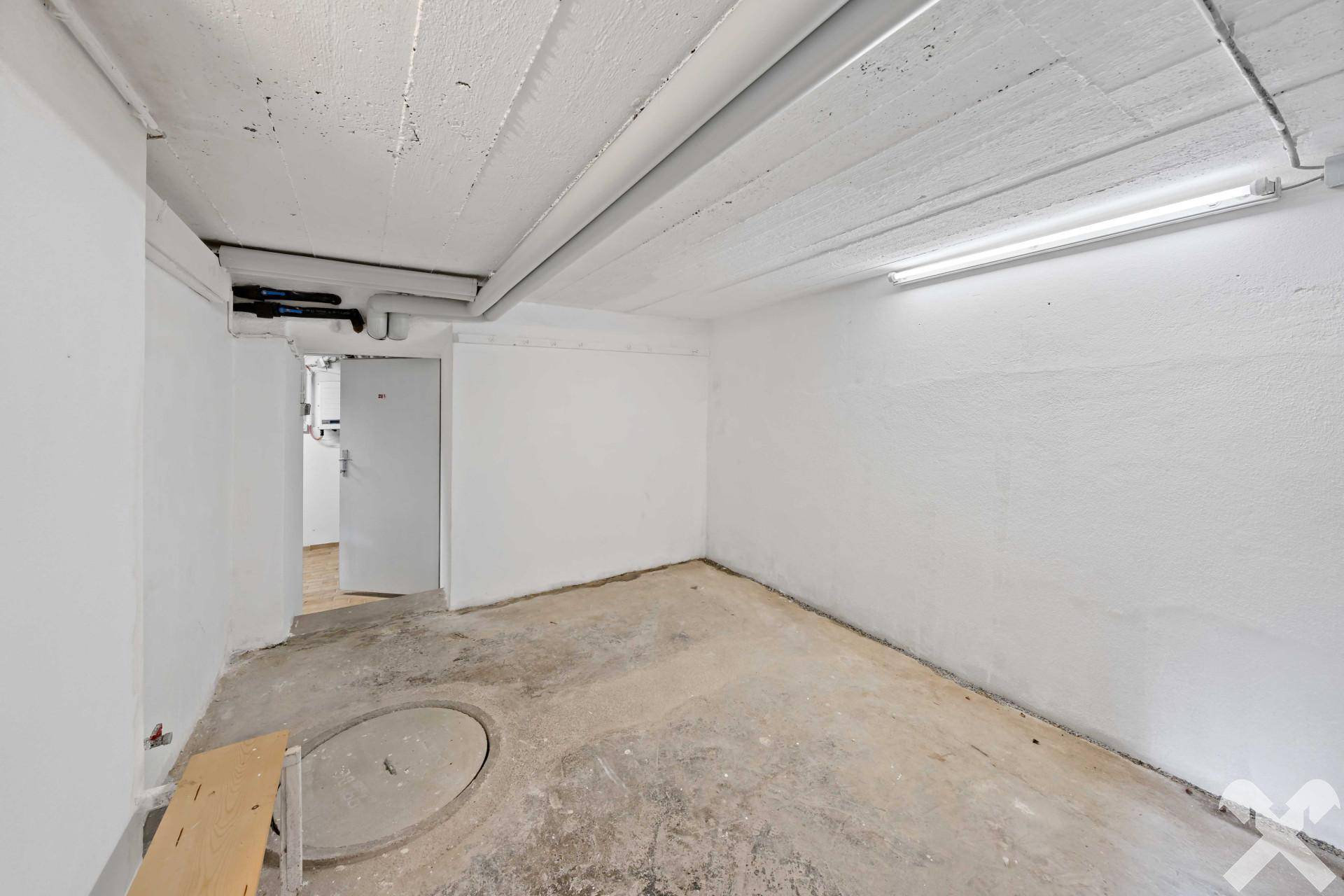 Leerer Kellerraum mit Betonboden und Zugang zu weiteren Untergeschossbereichen.
