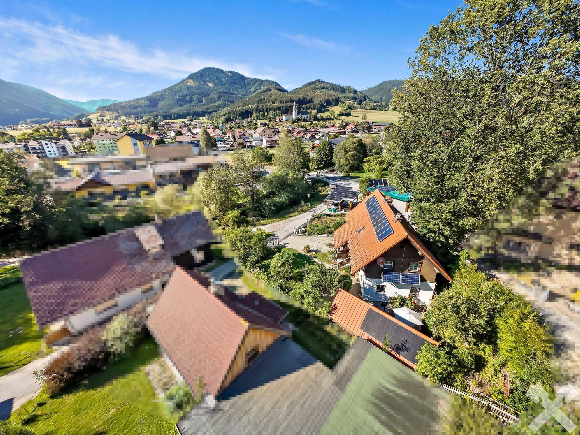 Weitläufige Luftaufnahme des Hauses mit Photovoltaikanlage und Blick auf das Dorf und die Berge.