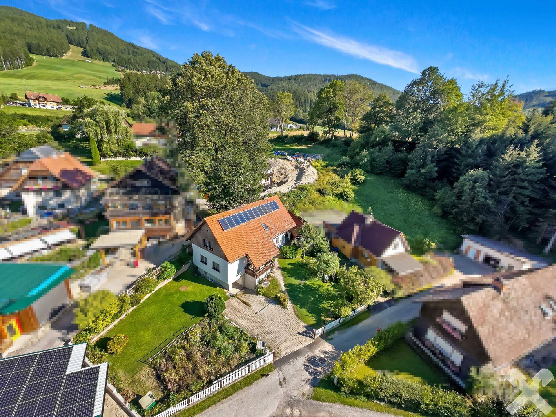 Luftaufnahme des Einfamilienhauses mit Photovoltaikanlage und der umliegenden grünen Landschaft.