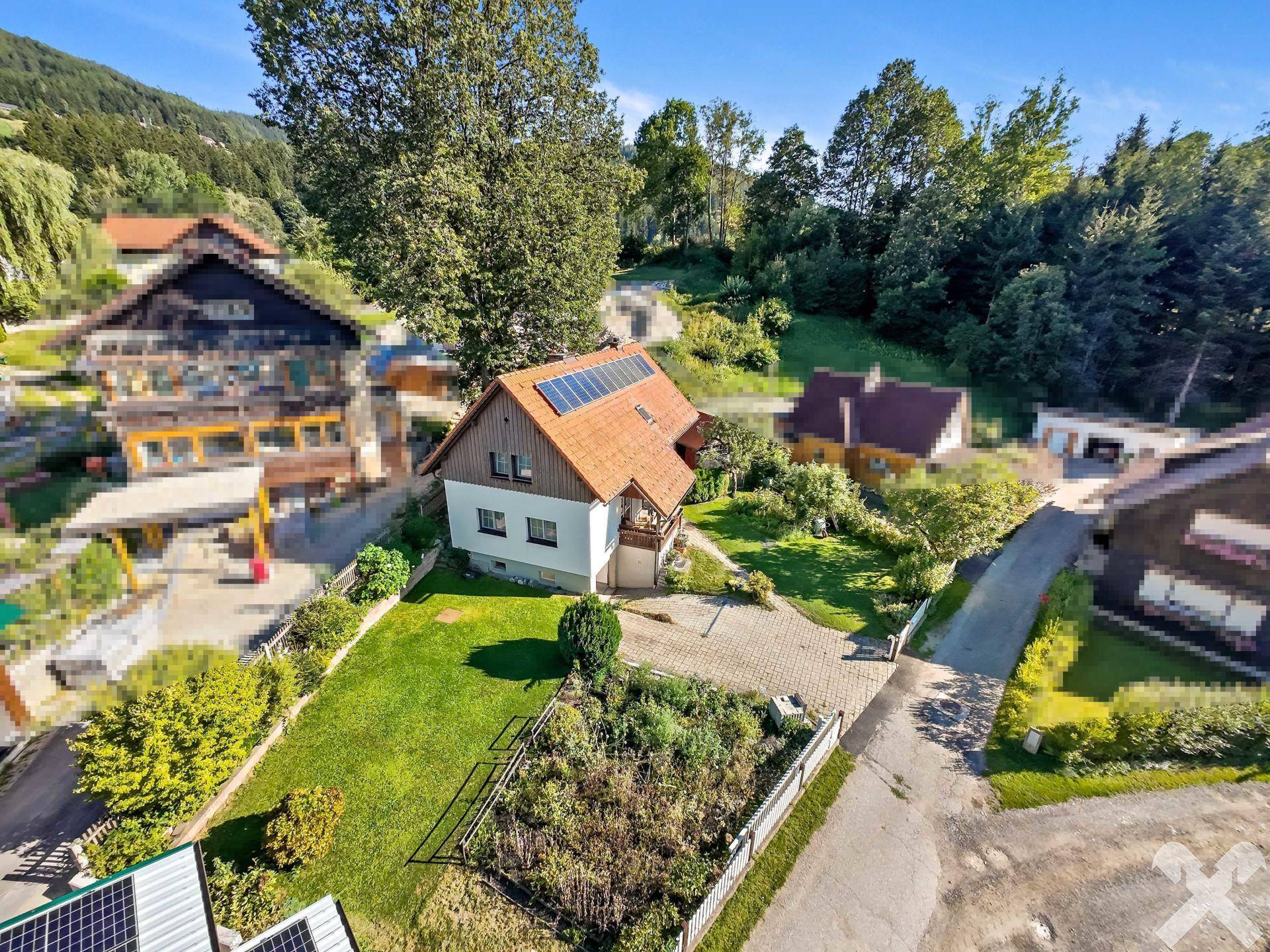 Haus mit rotem Ziegeldach, Photovoltaikmodulen und großem Garten in ländlicher Umgebung.