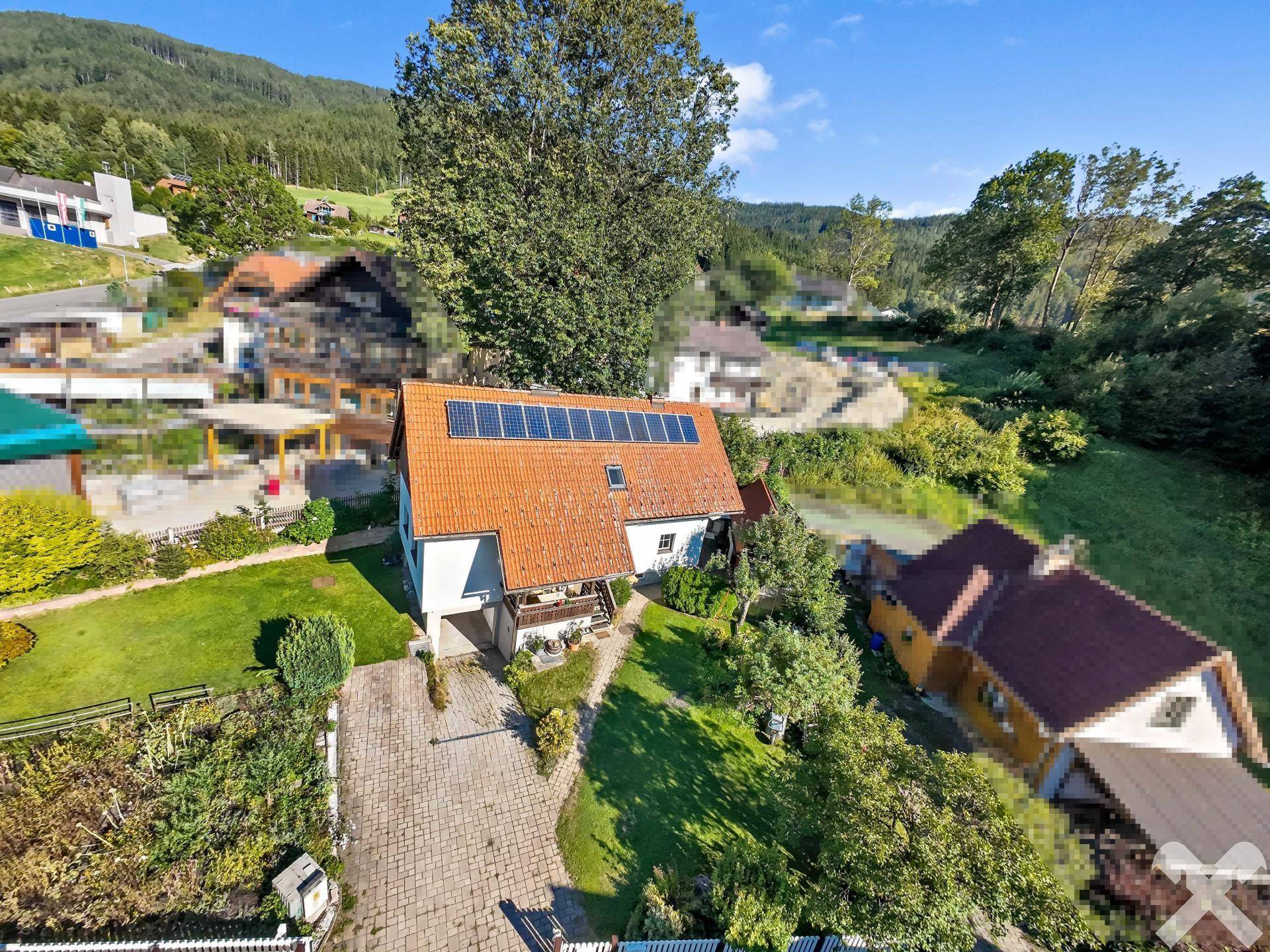 Luftaufnahme eines Einfamilienhauses mit Photovoltaikanlage, gepflasterter Auffahrt und grüner Umgebung.