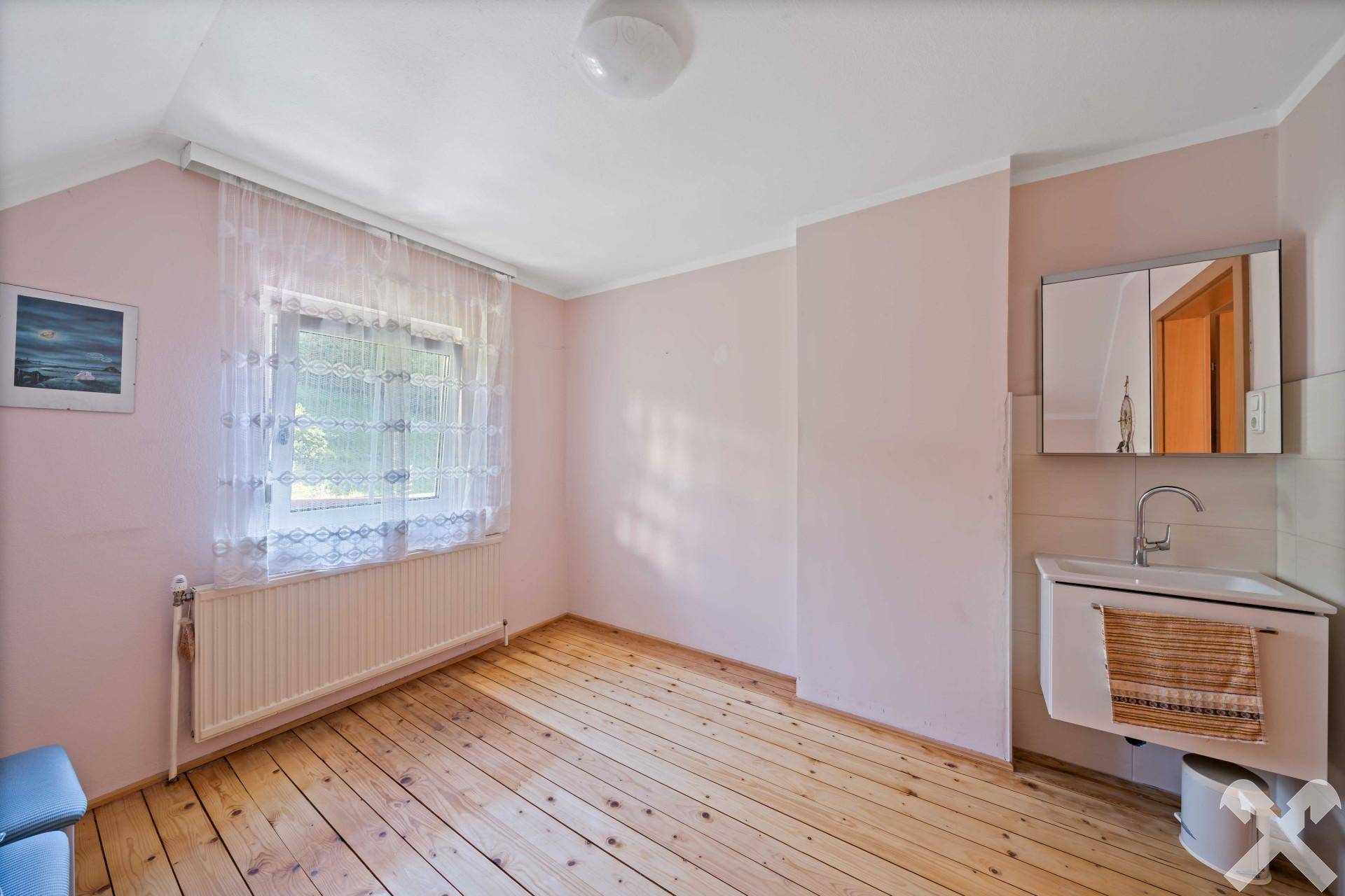 Schlafzimmer mit Waschbecken, Spiegelschrank und Holzdielenboden in zartem Rosa.
