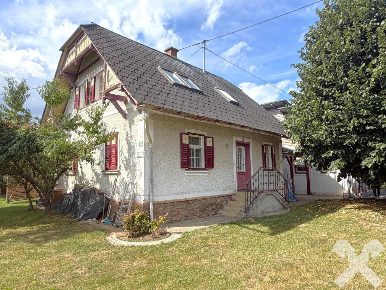 Vorderansicht des traditionellen Hauses mit roten Fensterläden, Dachfenstern und einem kleinen Vorgarten.