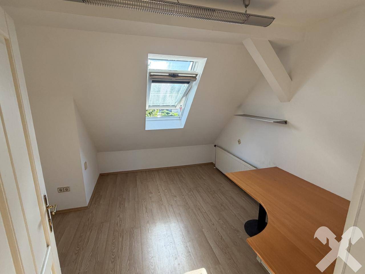 Helles Dachzimmer mit Laminatboden, Dachfenster und einem Schreibtisch.
