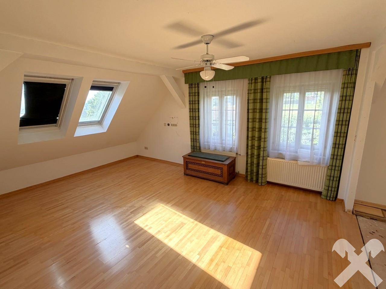 Geräumiges Schlafzimmer im Dachgeschoss mit Holzparkett, Dachfenstern und Deckenventilator.