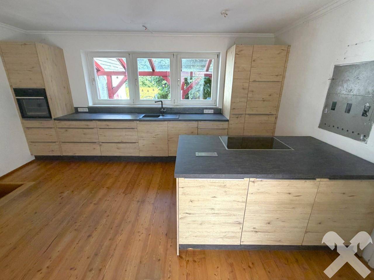 Neu installierte Küche mit hellen Holzfronten, dunkler Arbeitsplatte und Kochinsel.