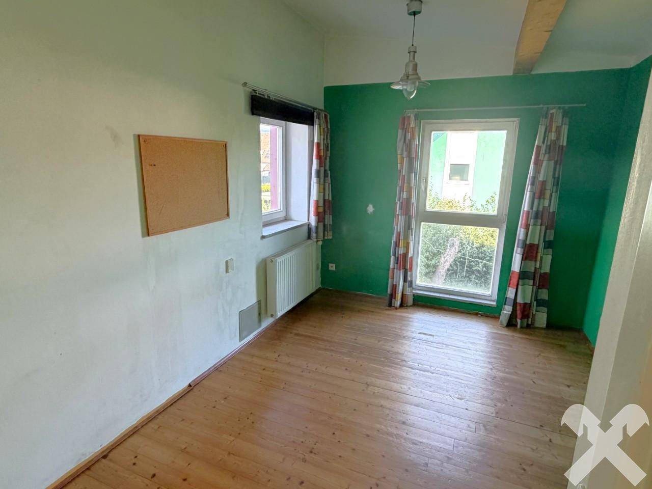 Geräumiges Zimmer mit Holzparkettboden, grünen Wänden und großen Fenstern.