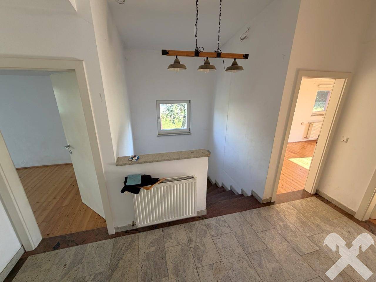 Heller Flur mit Steinfliesenboden, Treppe zum Obergeschoss und kleinem Fenster.