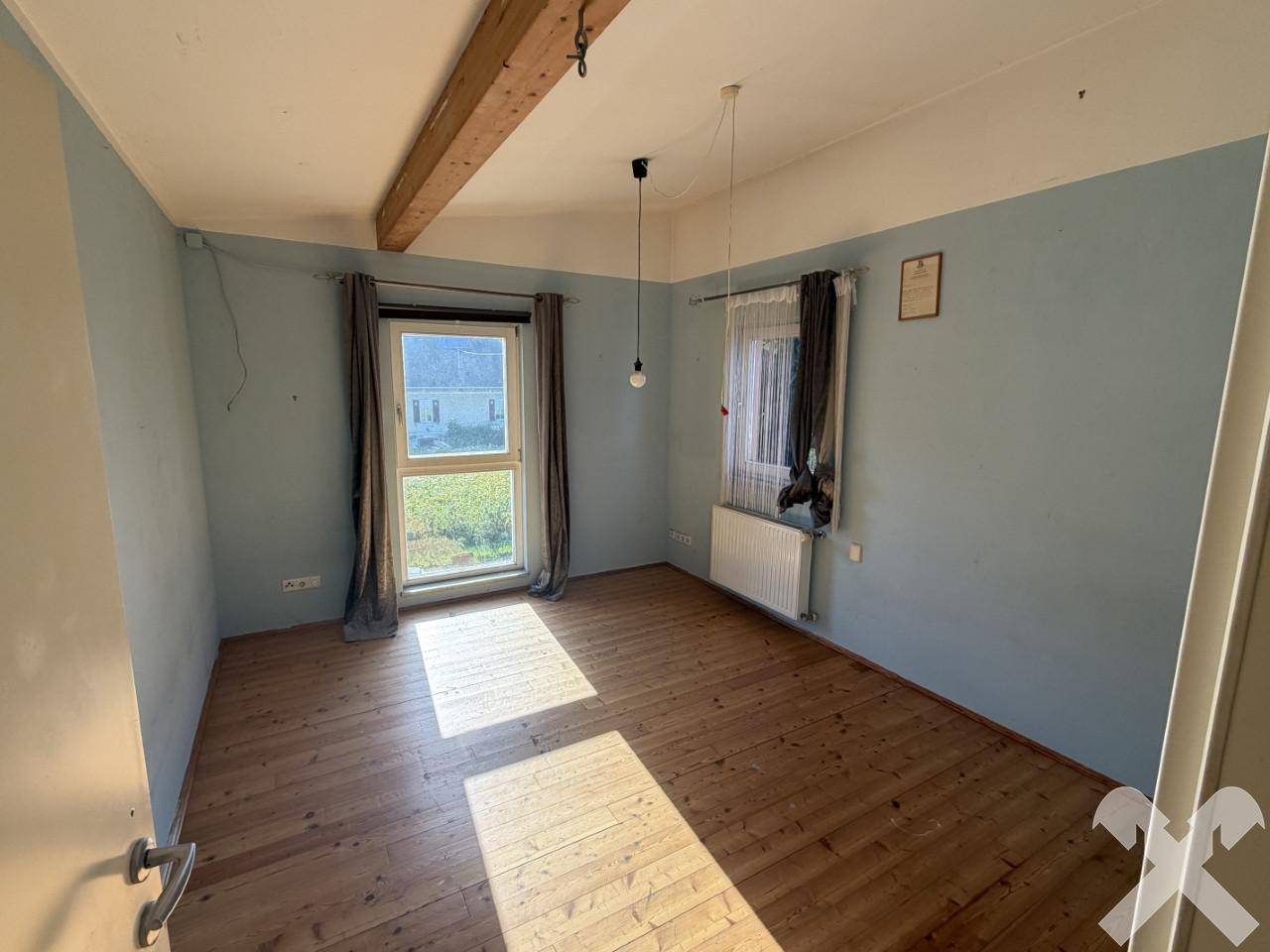 Helles Zimmer mit blauen Wänden, Holzdielenboden und sichtbarem Deckenbalken, ideal als Schlafzimmer.