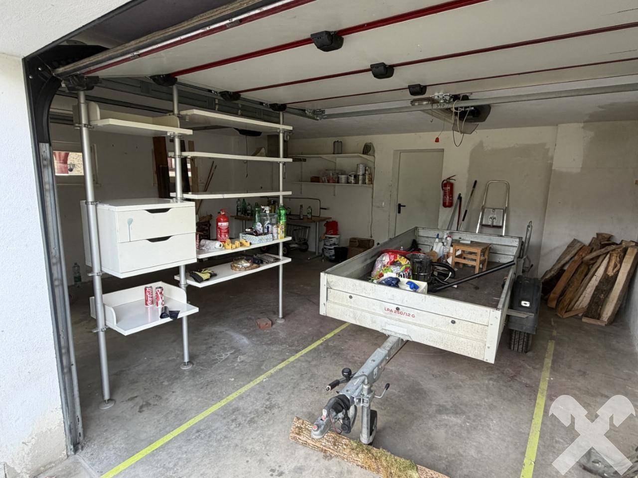 Geräumige Garage mit Betonboden, Regalen und einem Anhänger, bietet viel Stauraum.