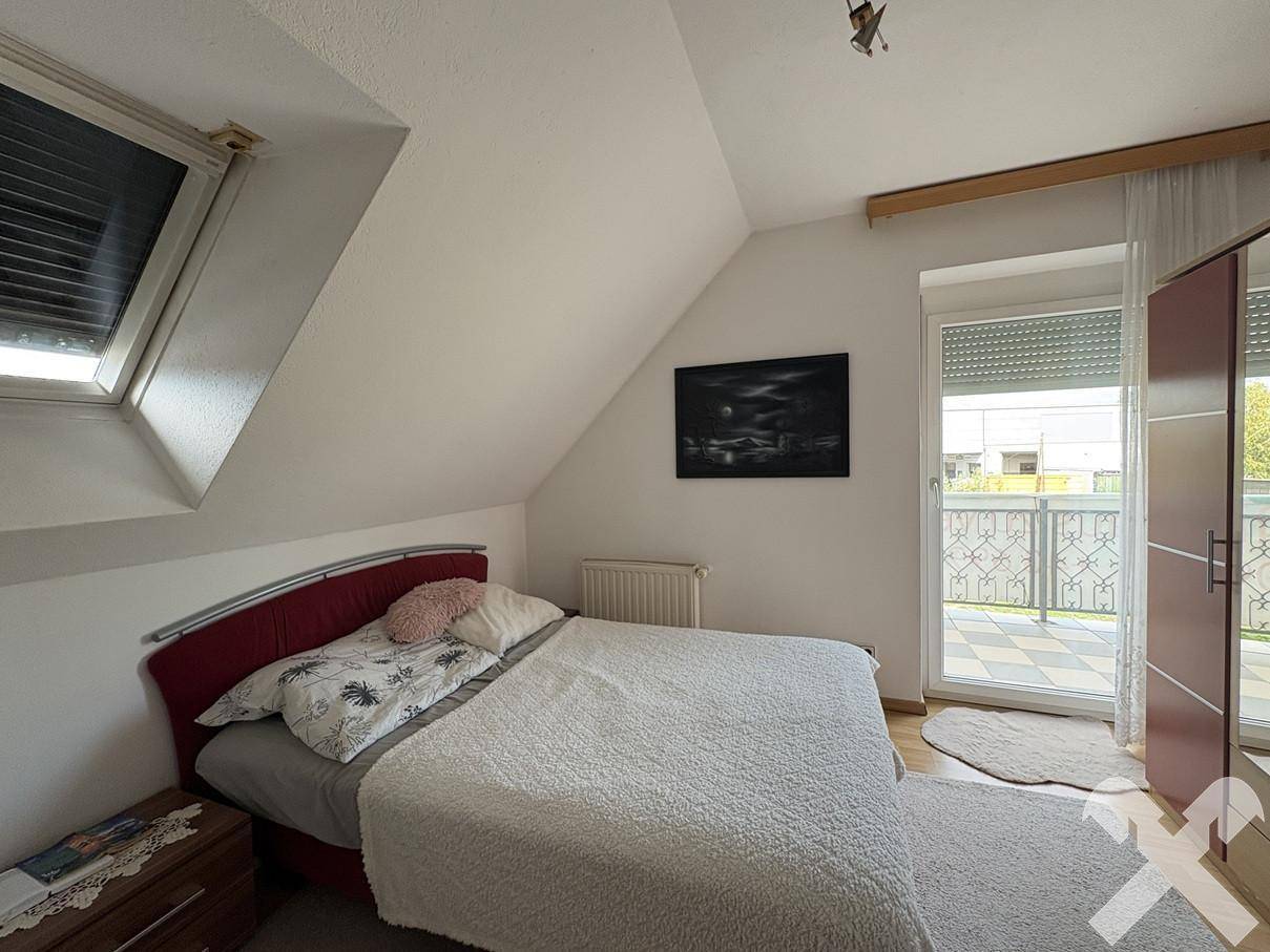 Schlafzimmer im Dachgeschoss mit Bett, Kleiderschrank, Dachfenster und Zugang zu einem Balkon.