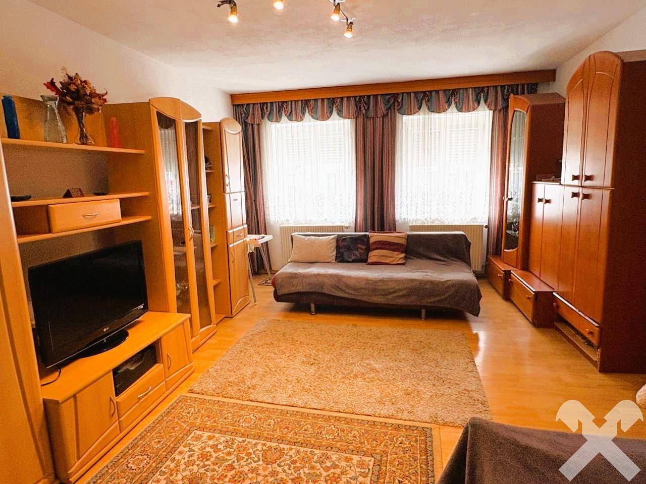 Wohnzimmer mit Holzmöbeln, einem Schlafsofa und einem Teppich auf Laminatboden.