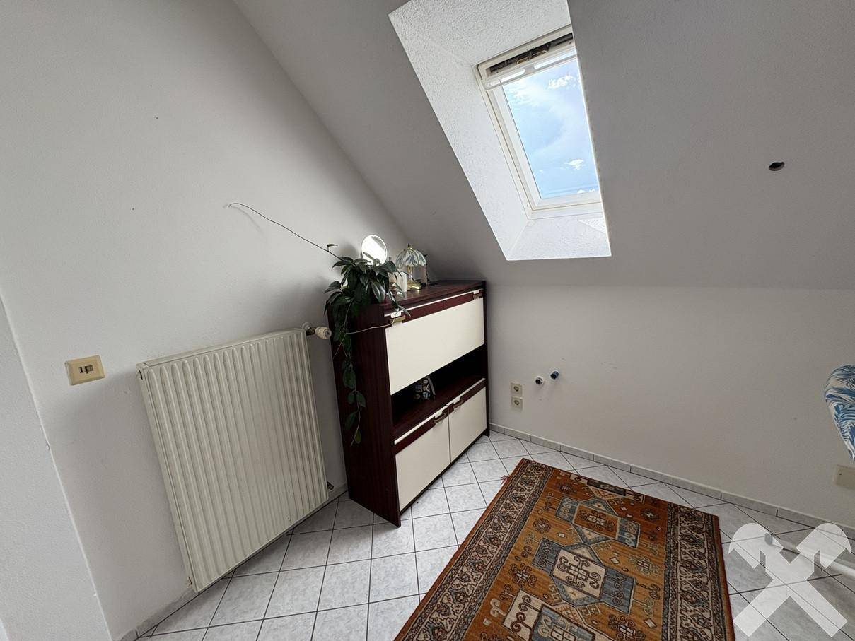 Kleiner Raum im Dachgeschoss mit gefliestem Boden, Heizkörper und einem Dachfenster.