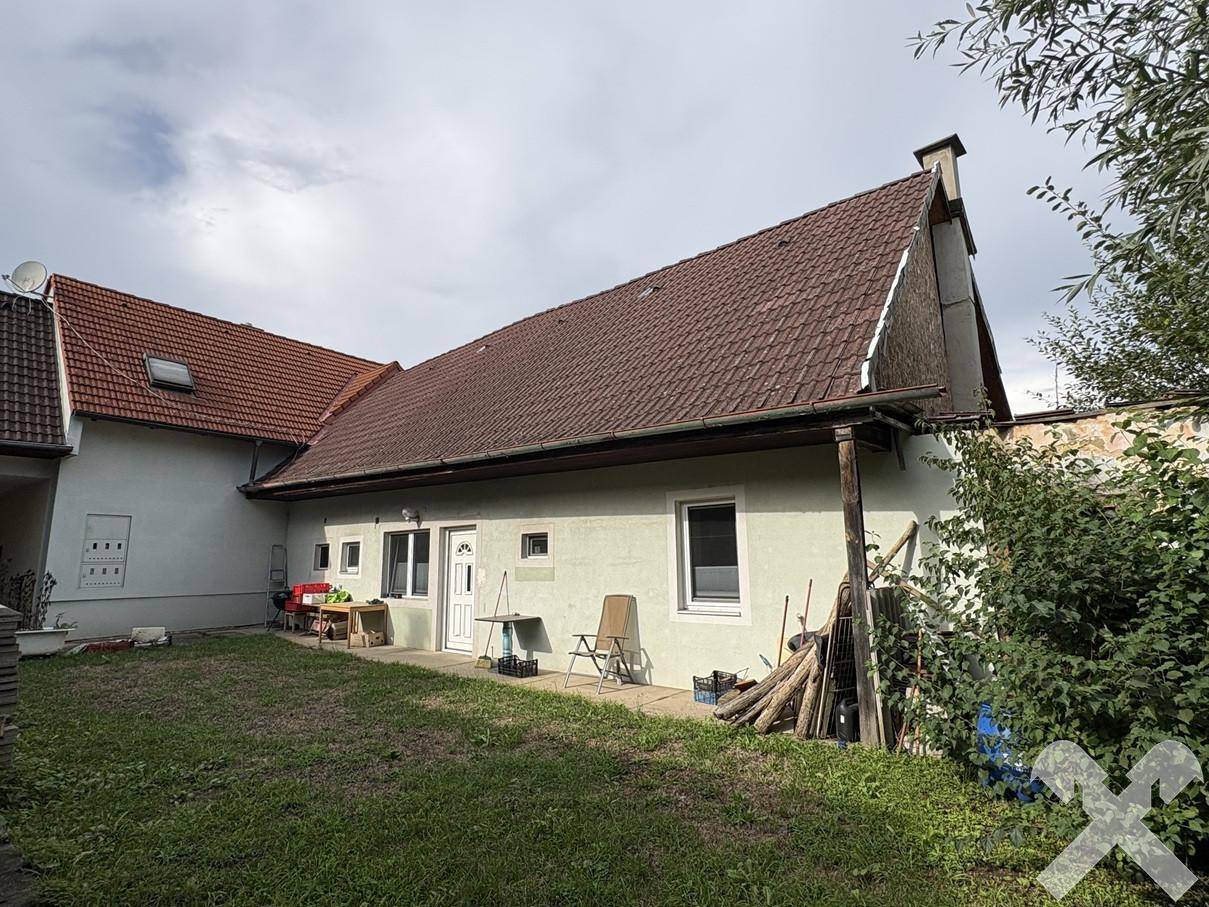 Rückseite des Hauses mit Garten, Rasenfläche und einem überdachten Bereich an der Fassade.