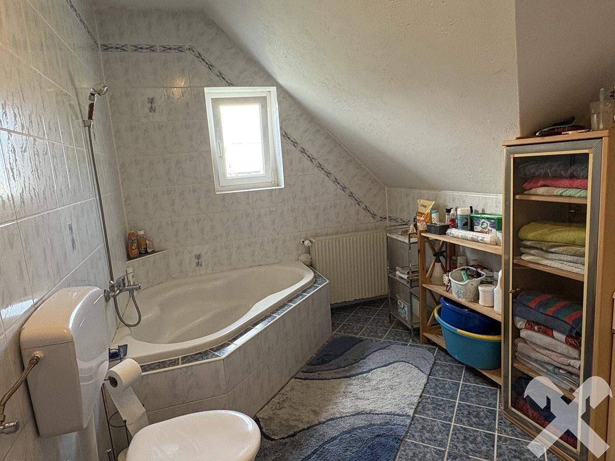 Badezimmer im Dachgeschoss mit Eckbadewanne, WC, gefliesten Wänden und einem Fenster.