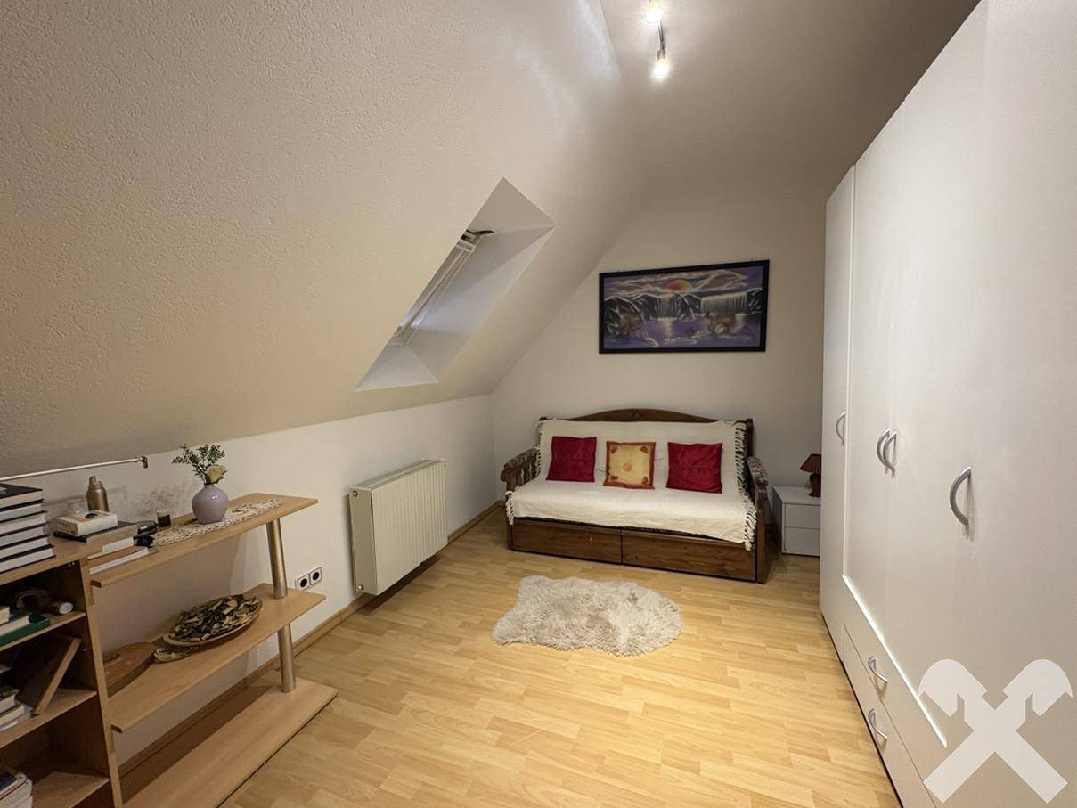 Dachzimmer mit Sofa, weißem Kleiderschrank, Regal und einem Dachfenster für natürliches Licht.