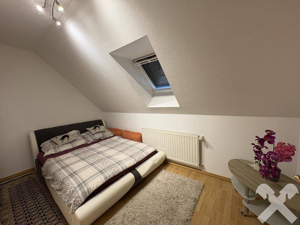 Weiteres Schlafzimmer im Dachgeschoss mit Bett, Teppich und einem Dachfenster.