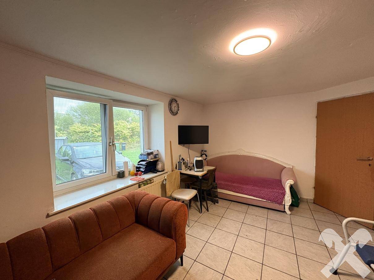 Heller Raum mit großem Fenster zum Garten, zwei Sofas und einem Fernseher auf gefliestem Boden.
