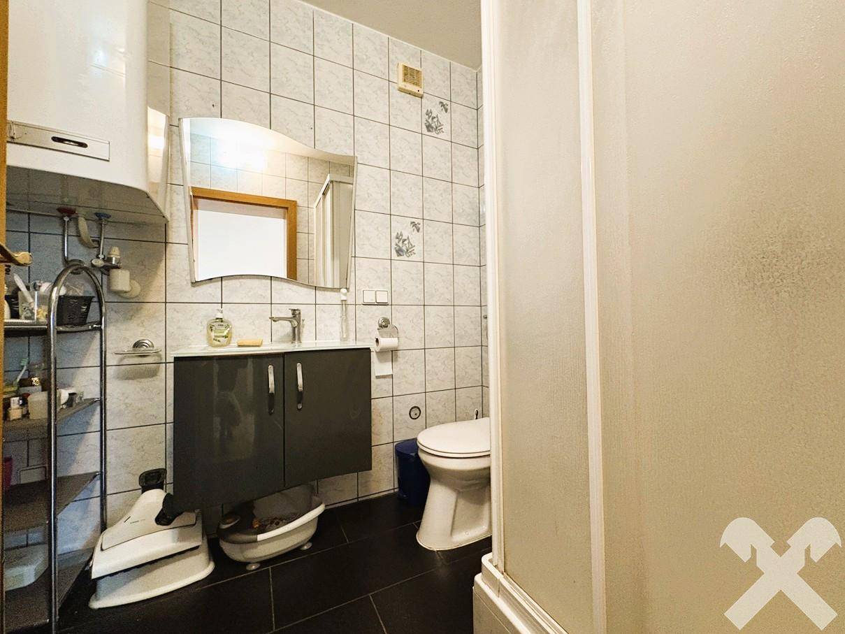Badezimmer mit Duschkabine, Waschbeckenunterschrank, WC und hell gefliesten Wänden.