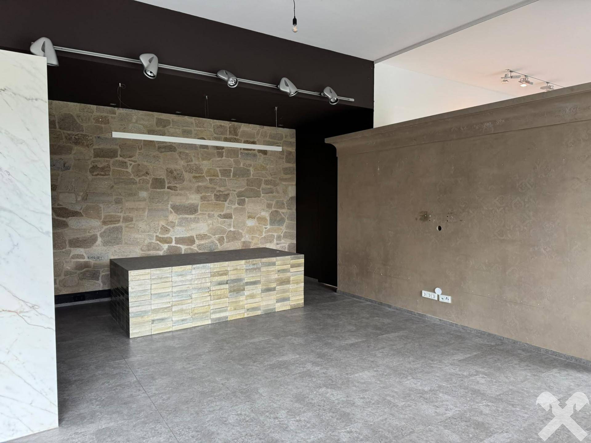 Detailansicht des Geschäftsraums mit Natursteinwand, Theke aus gestapeltem Stein und Schienenbeleuchtung.
