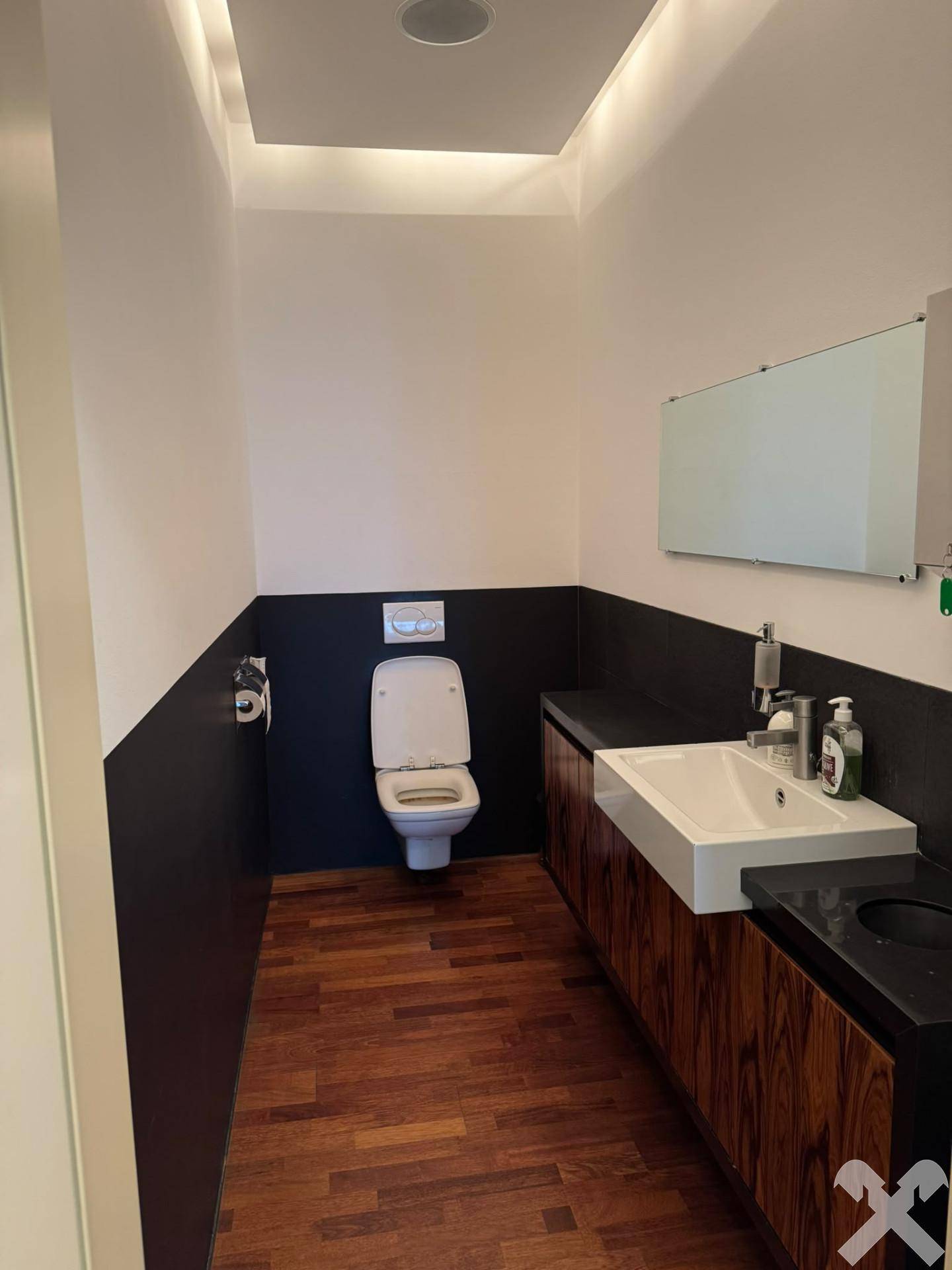 Modernes Badezimmer oder Gäste-WC mit Holzdielenboden, Wand-WC, weißem Waschbecken und Holzunterschränken.