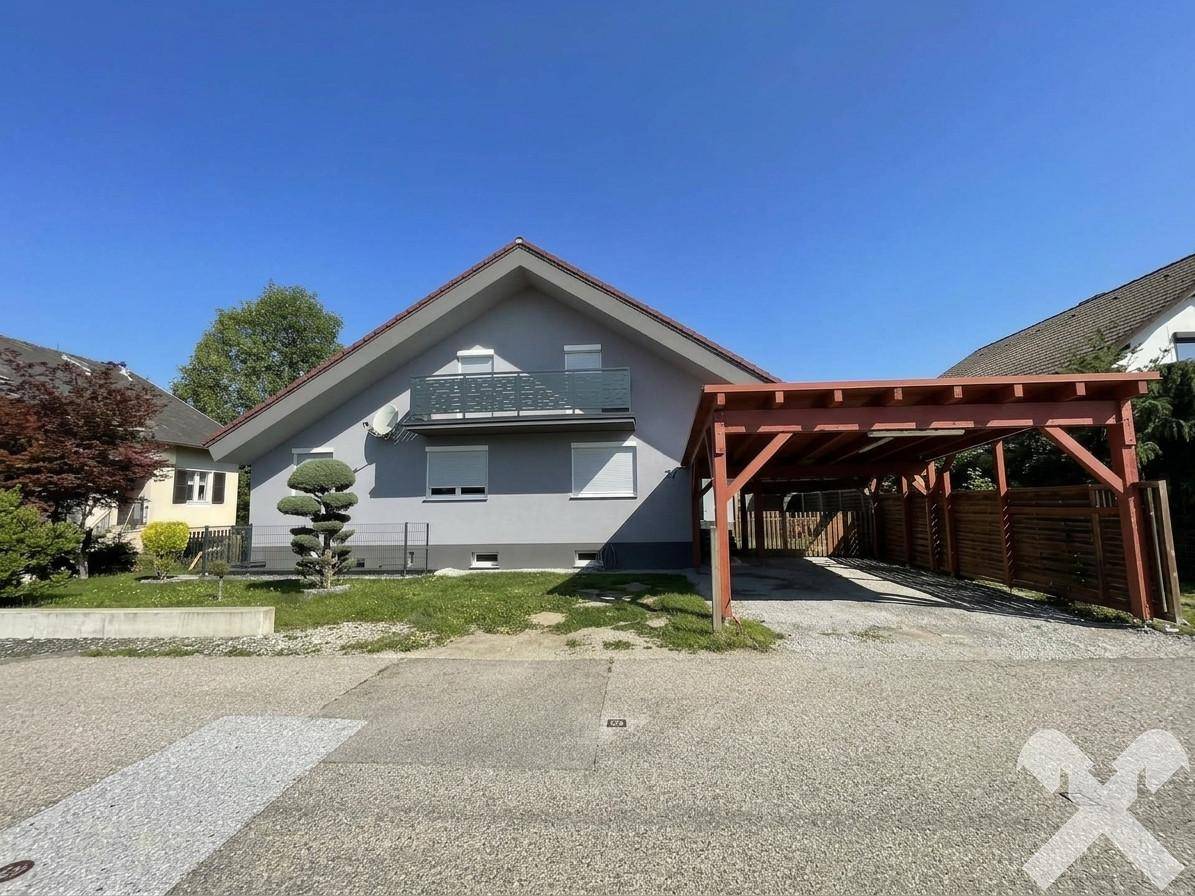 Einfamilienhaus mit Satteldach, kleinem Balkon und einem Holzcarport auf dem Grundstück.