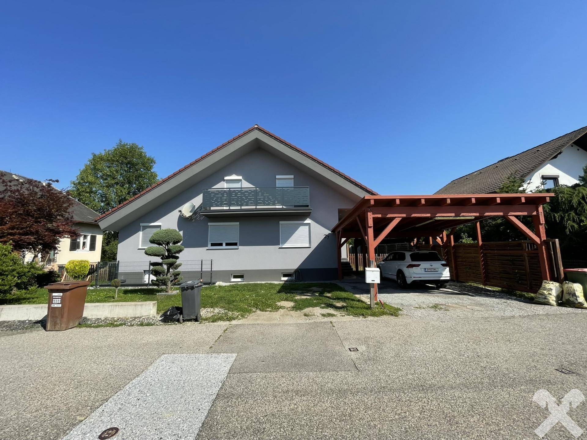 Gepflegtes Einfamilienhaus mit Carport und parkendem Auto vor der grauen Fassade.