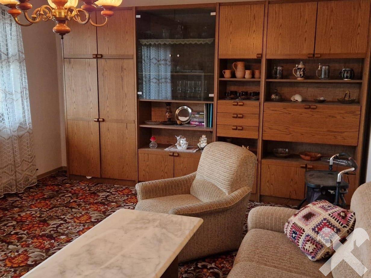 Wohnzimmer mit gemustertem Teppichboden, Holzschränken und bequemen Sitzmöbeln.