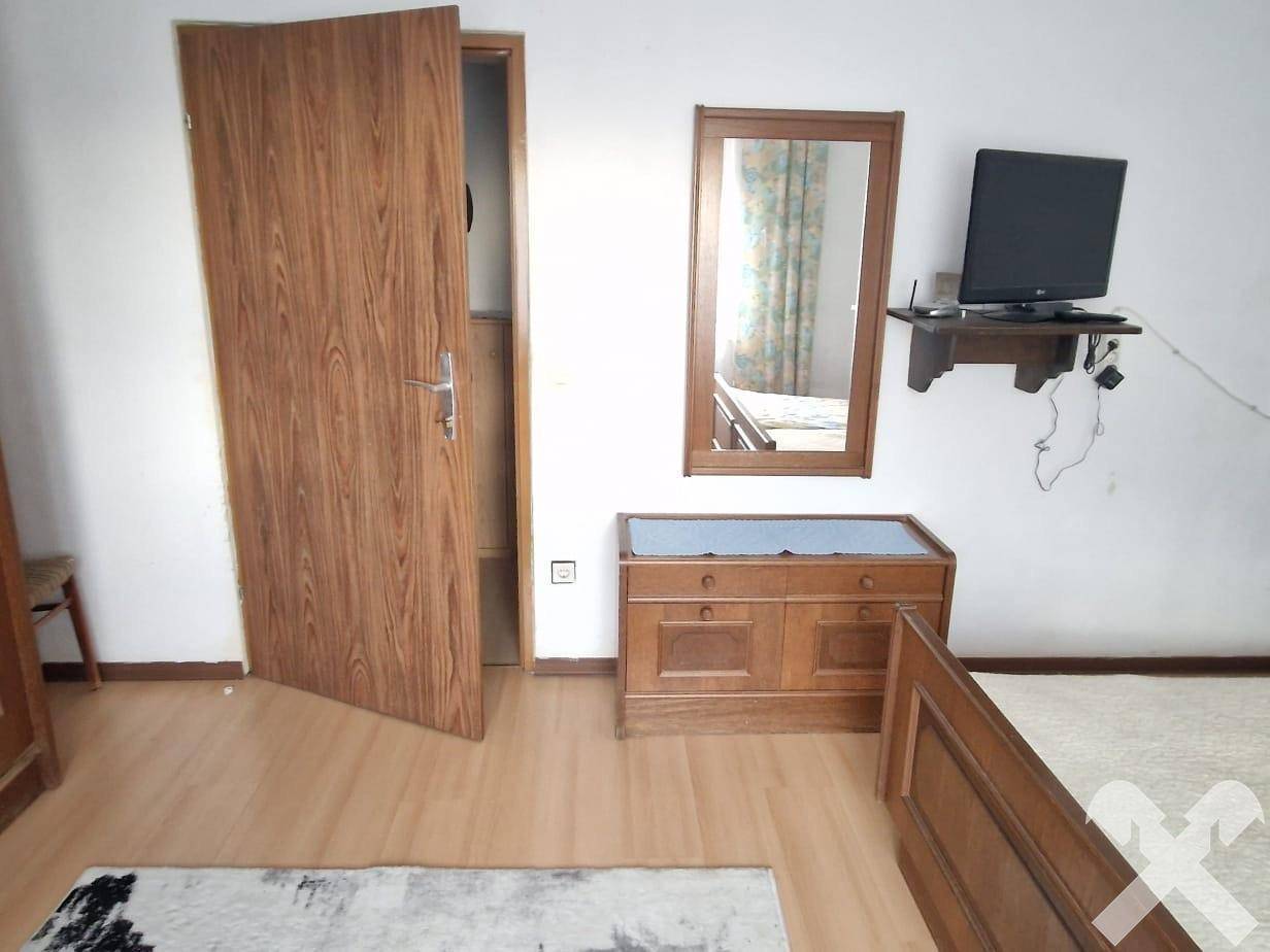 Schlafzimmer mit Holzbettrahmen, Spiegel und kleinem Fernseher an der Wand.