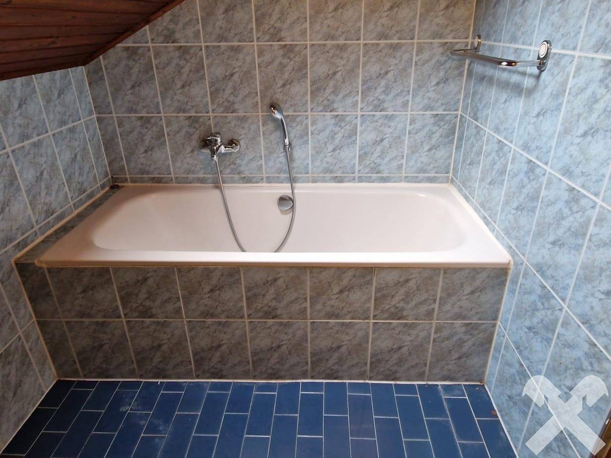 Badezimmer mit eingebauter Badewanne und blauen Fliesen, unter einer Dachschräge gelegen.