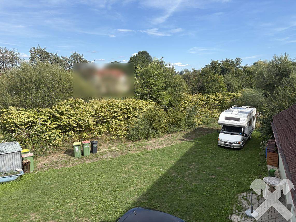 Blick von oben auf den Garten mit Rasenfläche, einem Wohnmobil und umgebender Vegetation.