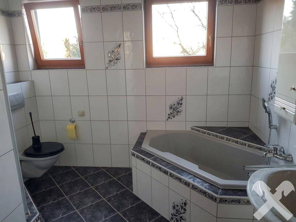 Badezimmer mit Eckbadewanne, Toilette und Fenster, hell gefliest mit dekorativen Akzenten.